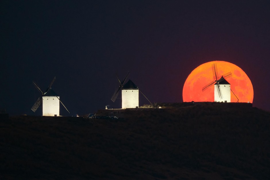 Polna luna nad mlini na veter v španskem mestu Consuegra je zasijala v svetlo oranžni barvi. Za več kliknite NAPREJ.