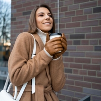 Ženska z rokavicami v rokah drži skodelico kave