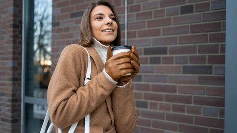 Ženska z rokavicami v rokah drži skodelico kave